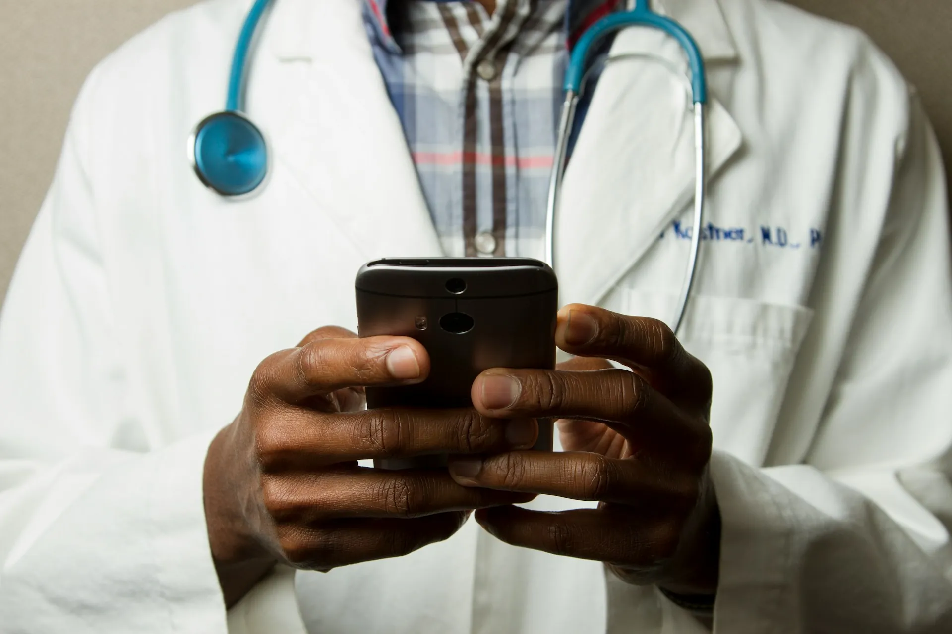 A health professional wearing a white coat and a stethoscope, holding their phone.