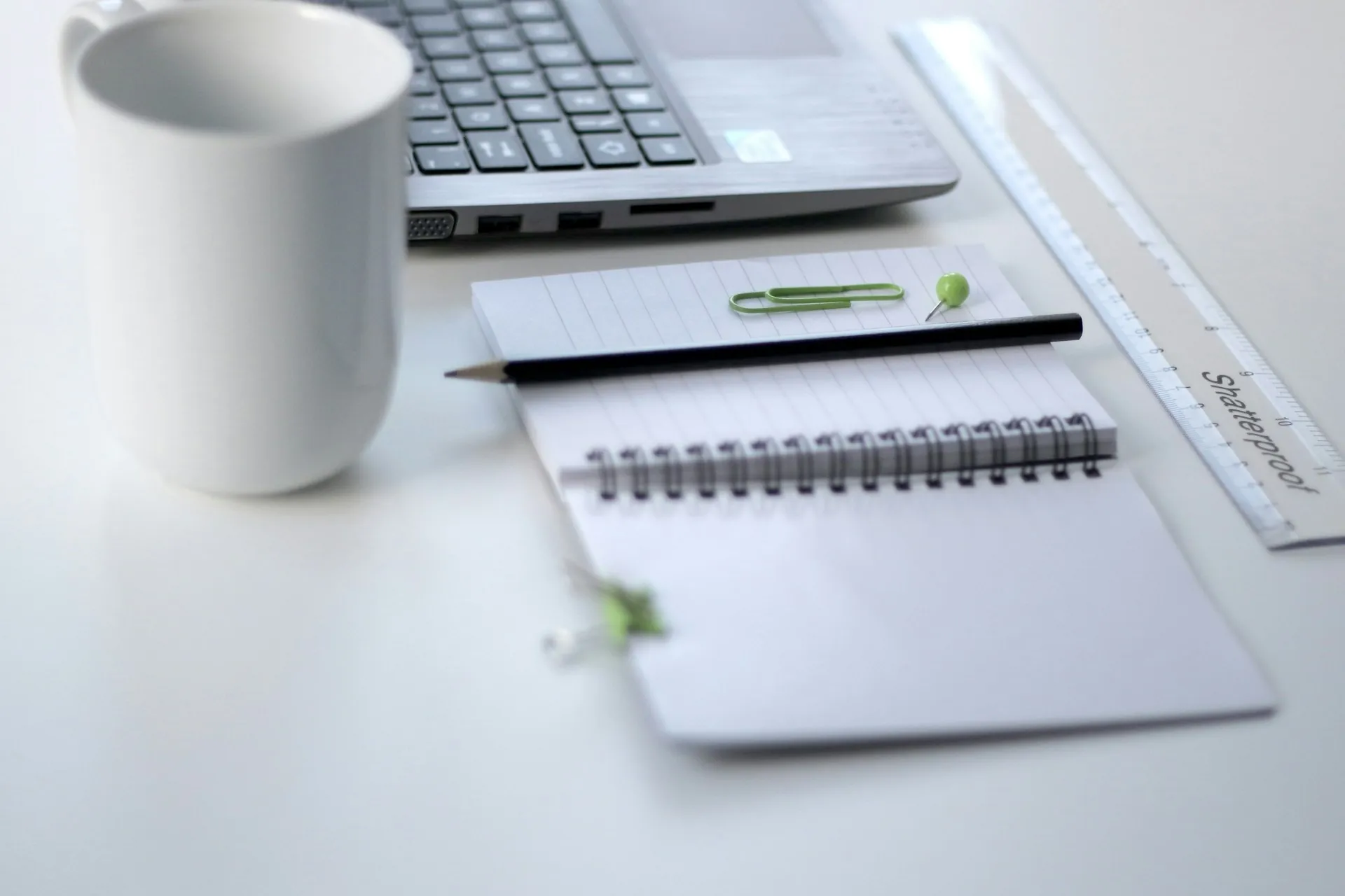 Un computer portatile, un quaderno, penne e una tazza di ceramica bianca su un tavolo. Time Tracking per Insegnanti.