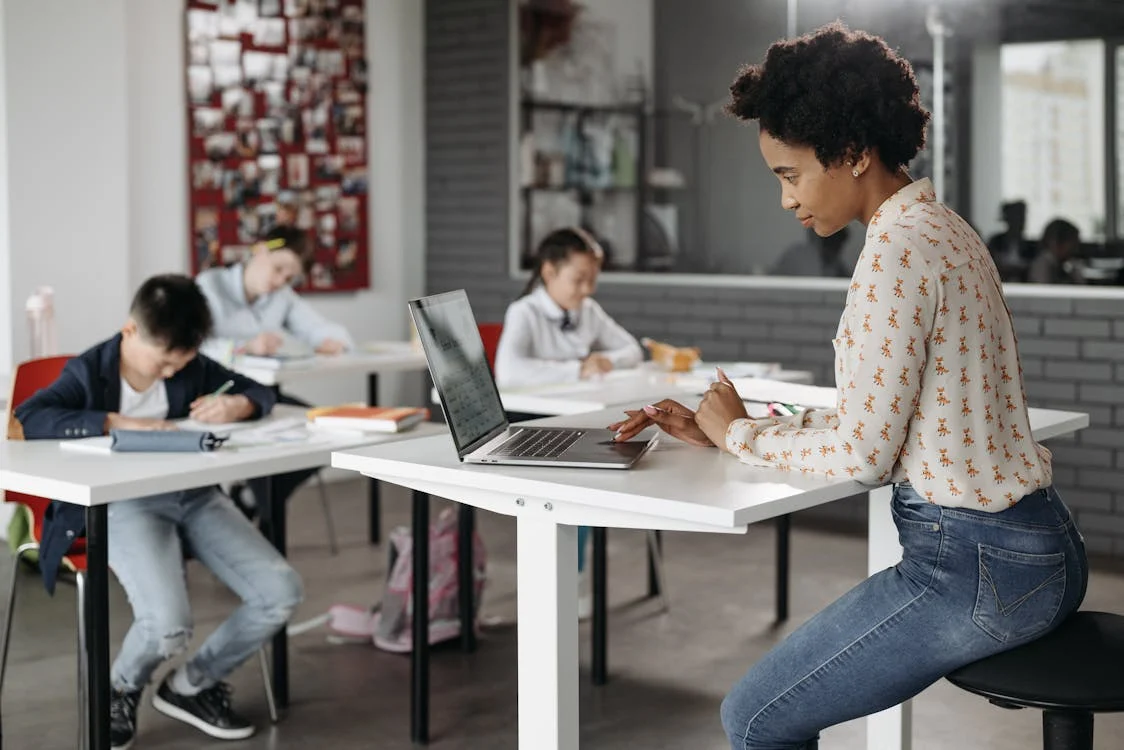 Un insegnante sul suo computer portatile mentre i suoi studenti sono impegnati.