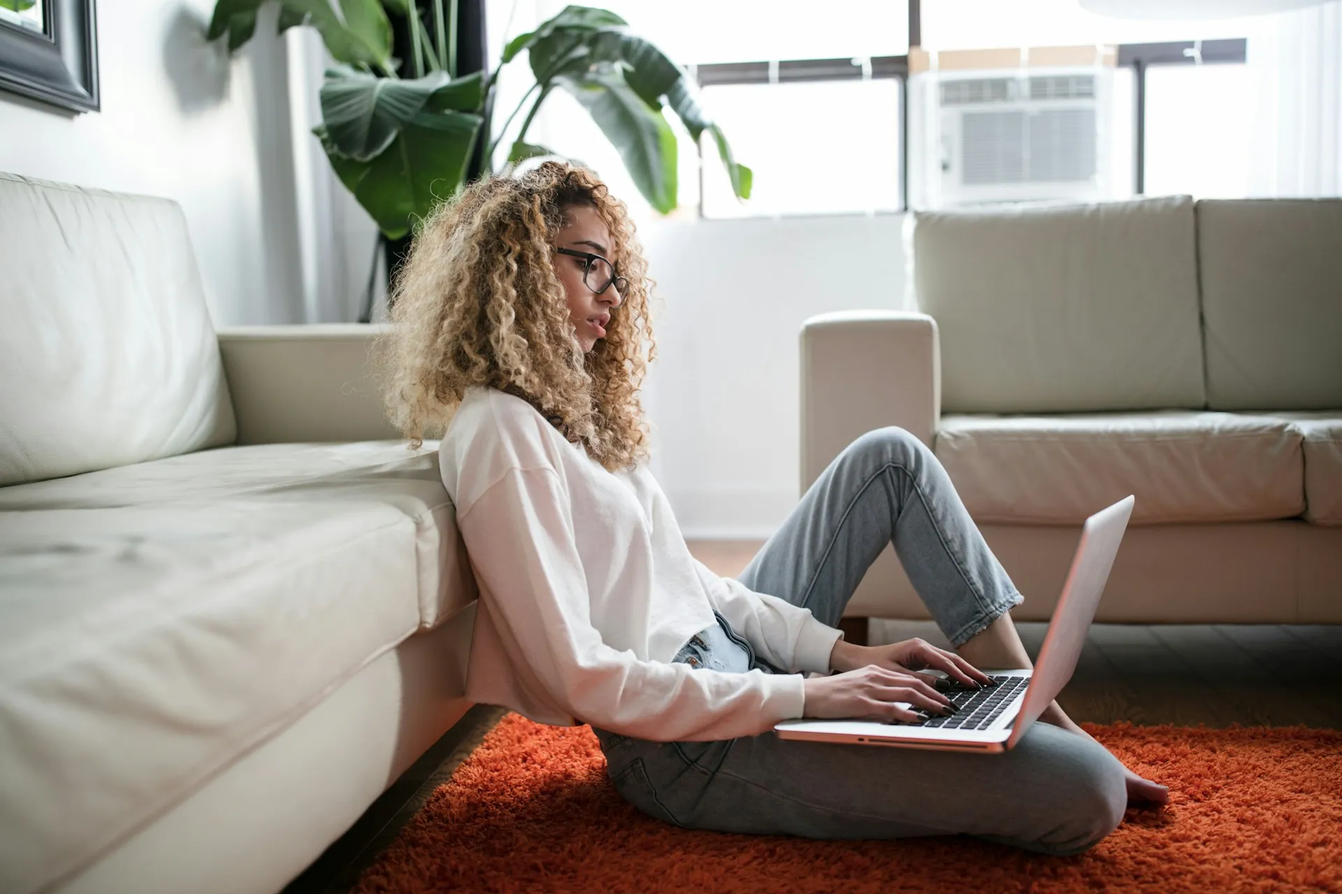 A woman working on her laptop while sitting on her living room floor.