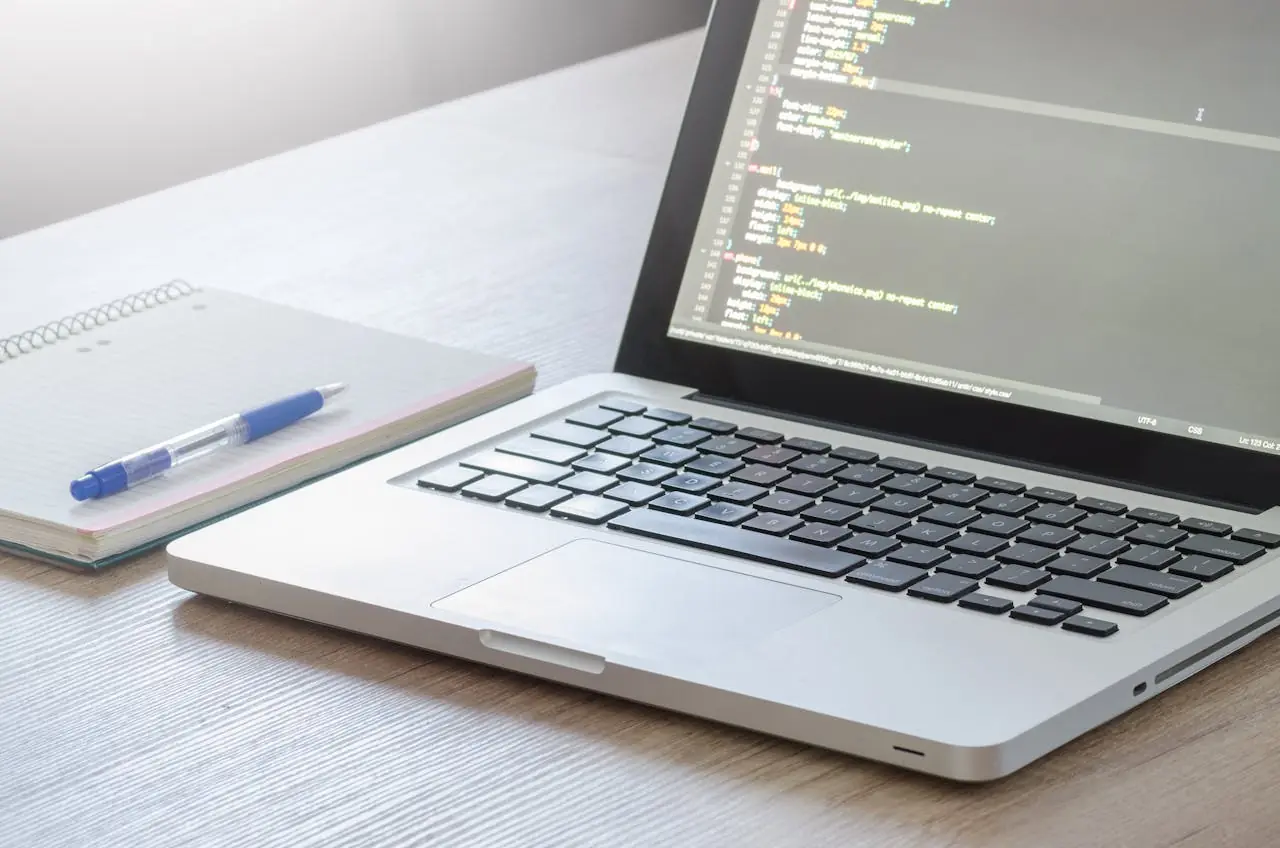 A compute with code displayed on its screen placed next to a notebook and a pen. Self-hosted time tracking software.