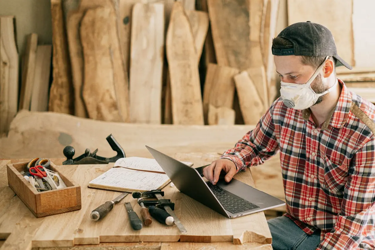 A construction site manger inside a workshop working on his laptop.