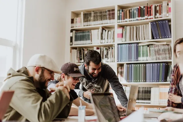 A group of employees laughing and working on their laptops at the office.