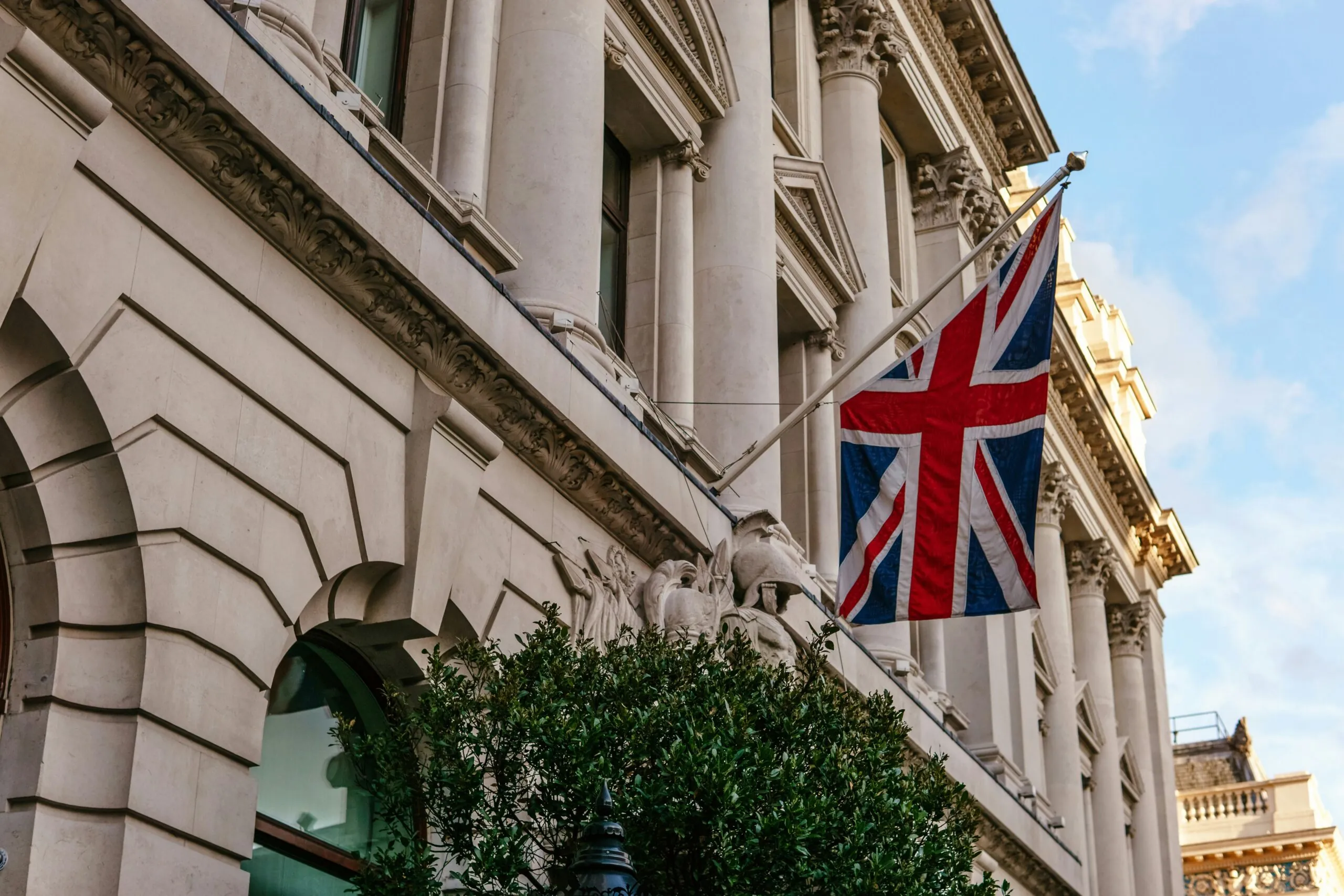  A Union Jack flag flying on a historic building with ornate architectural details and a clear blue sky in the background.